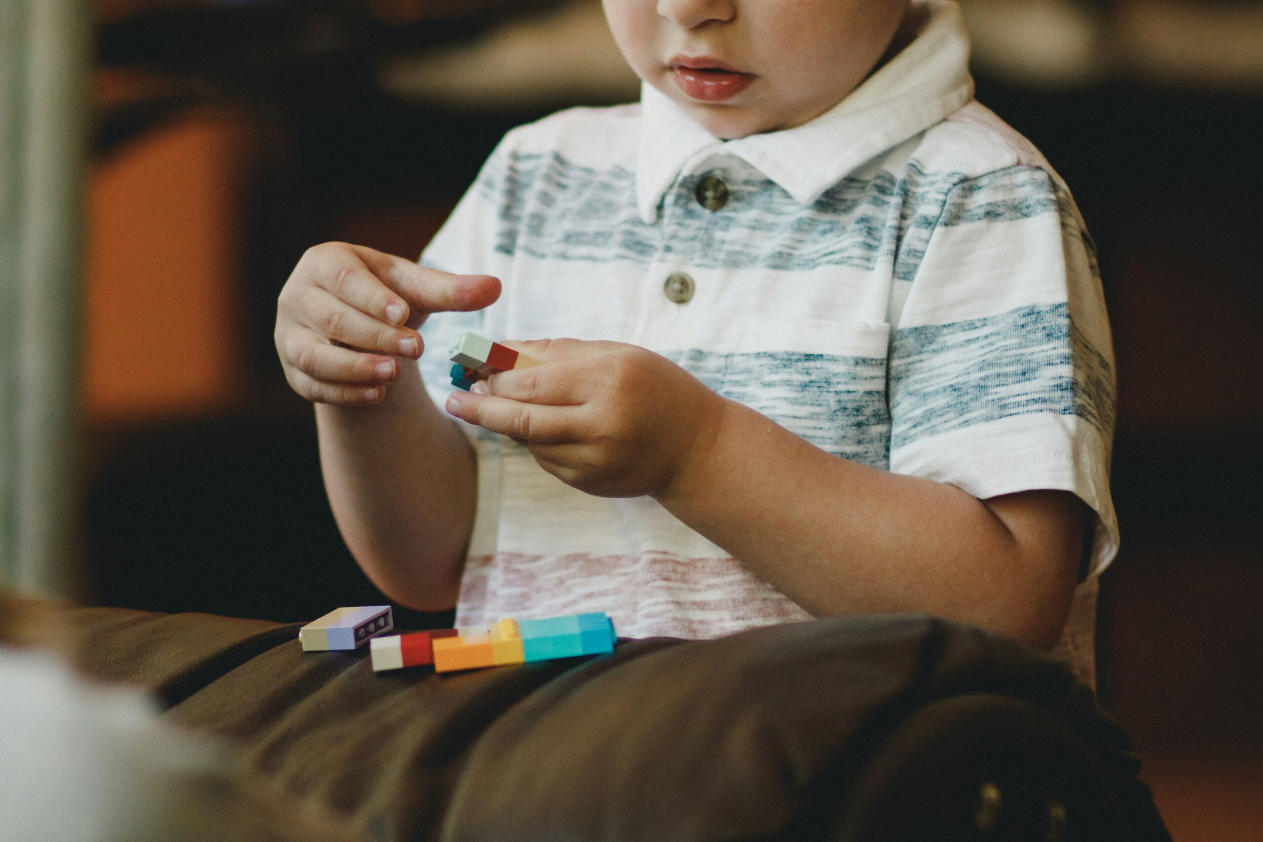 A young boy, who has autism, playing with blocks in a living room while his parents watch with hope and excitement.