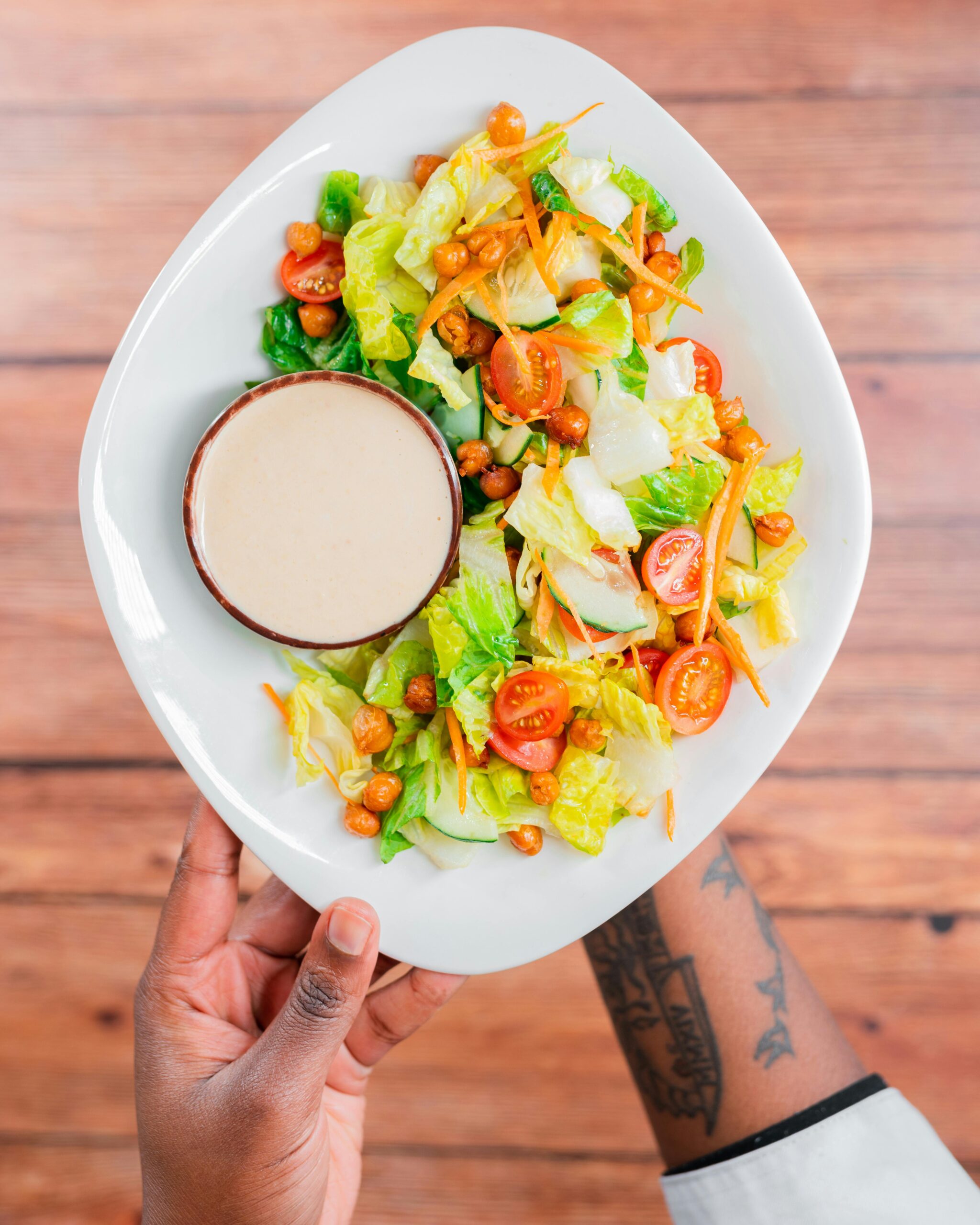 A person holding a plate of salad with a side of simple blender salad dressing.