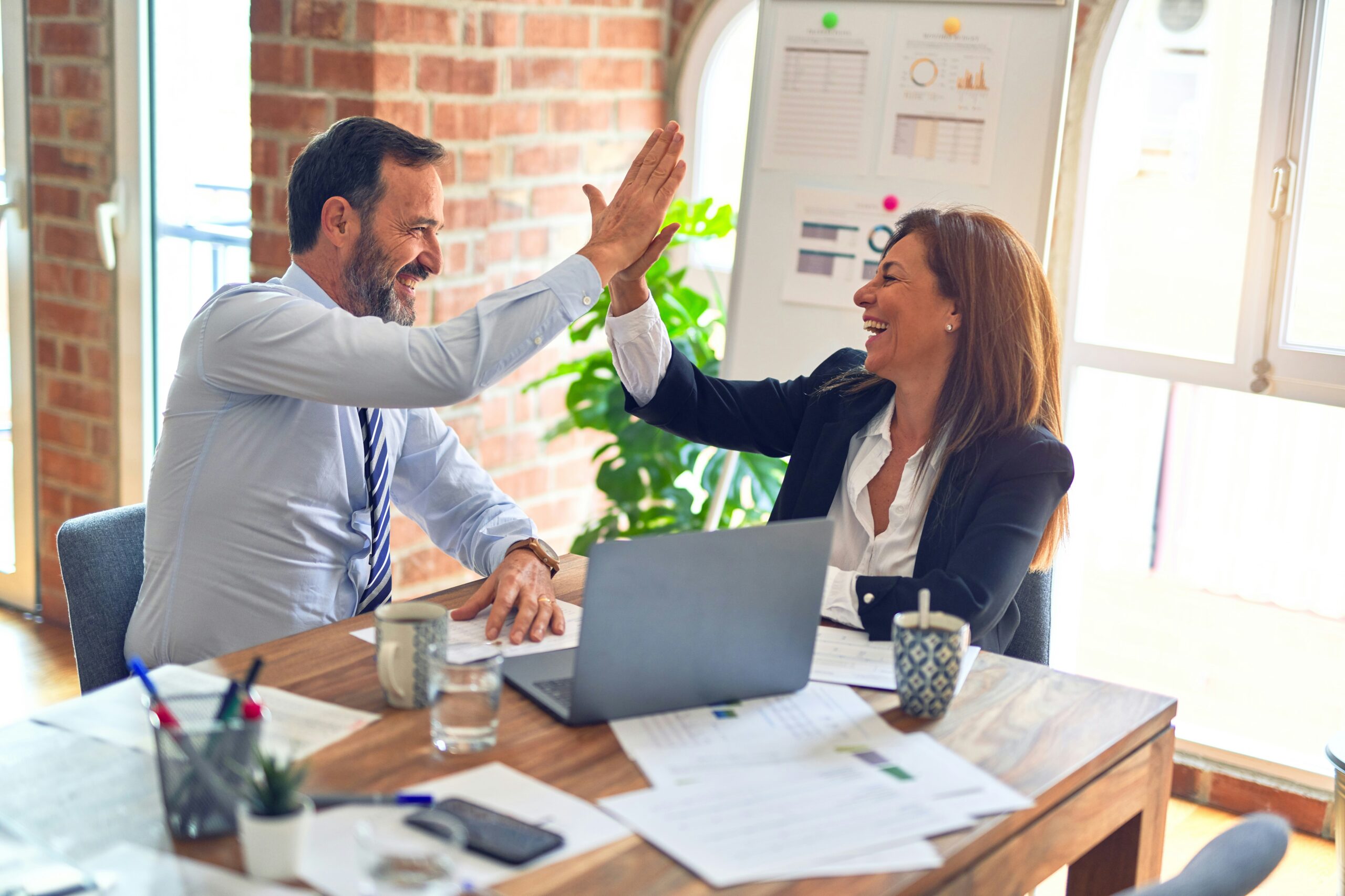 Two professionals discussing business insurance giving each other a high-five in an office setting.